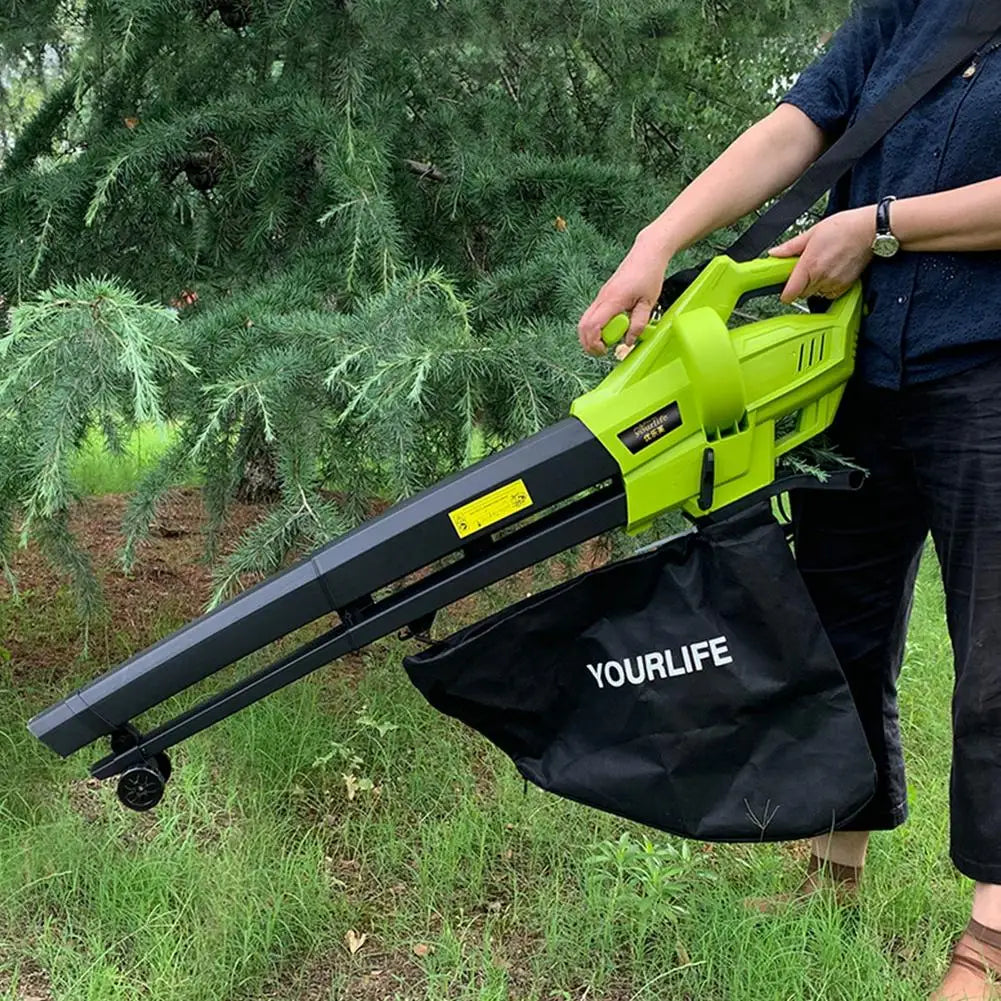 Person using a lime green leaf blower and vacuum combo with a black collection bag labeled "YOURLIFE" in a grassy area near pine trees.
