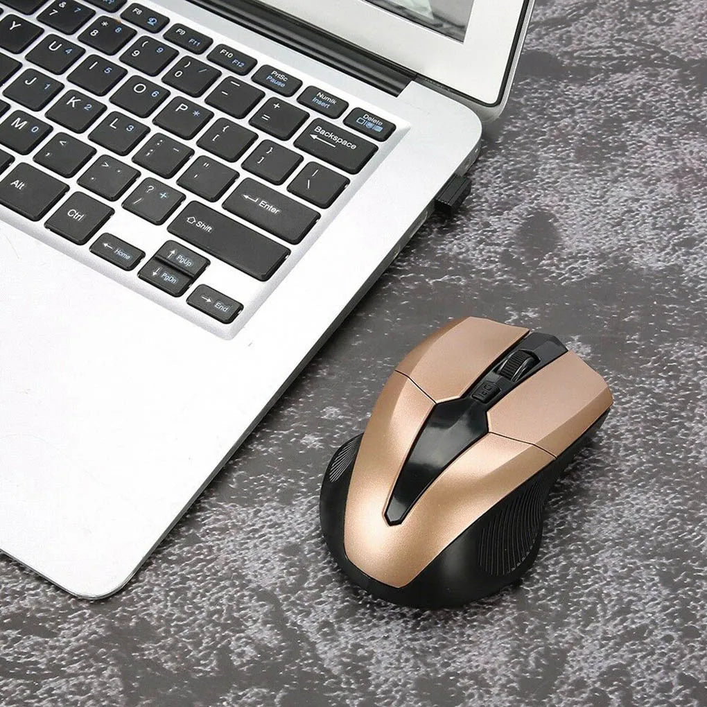 A gold and black wireless mouse sits on a textured gray surface next to an open laptop with a silver body and black keys.