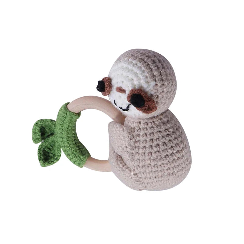 Crocheted sloth with a wooden ring, featuring green fabric leaves. The sloth has a happy face and embraces the ring, offering a soft and natural play toy for babies.