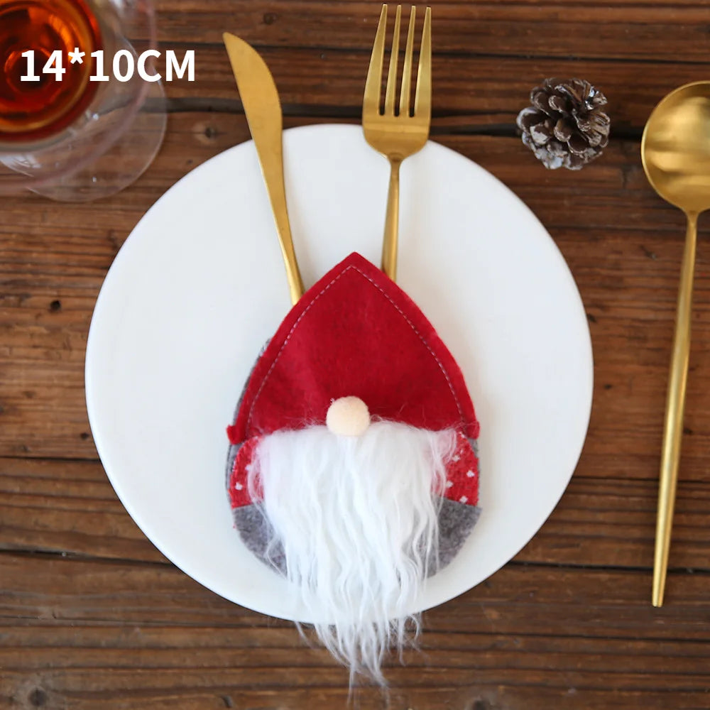 A festive table setting with a white plate, featuring a gnome-shaped cutlery holder with a red hat and white beard, holding a gold fork and knife. A pine cone and drink are nearby.