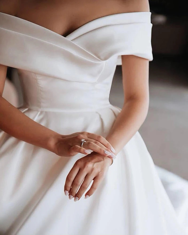Bride in an elegant white off-the-shoulder wedding dress, with hands gracefully clasped, highlighting a delicate engagement ring.