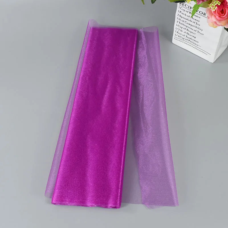 A vibrant pink velvet and sheer lilac fabric folded neatly on a gray surface, with flowers and a decorative box partially visible in the background.