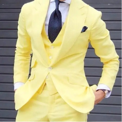 Person in a bright yellow suit with a matching vest and a dark tie, standing against a gray shutter backdrop. Hands are in pockets, and a watch is visible on the wrist.