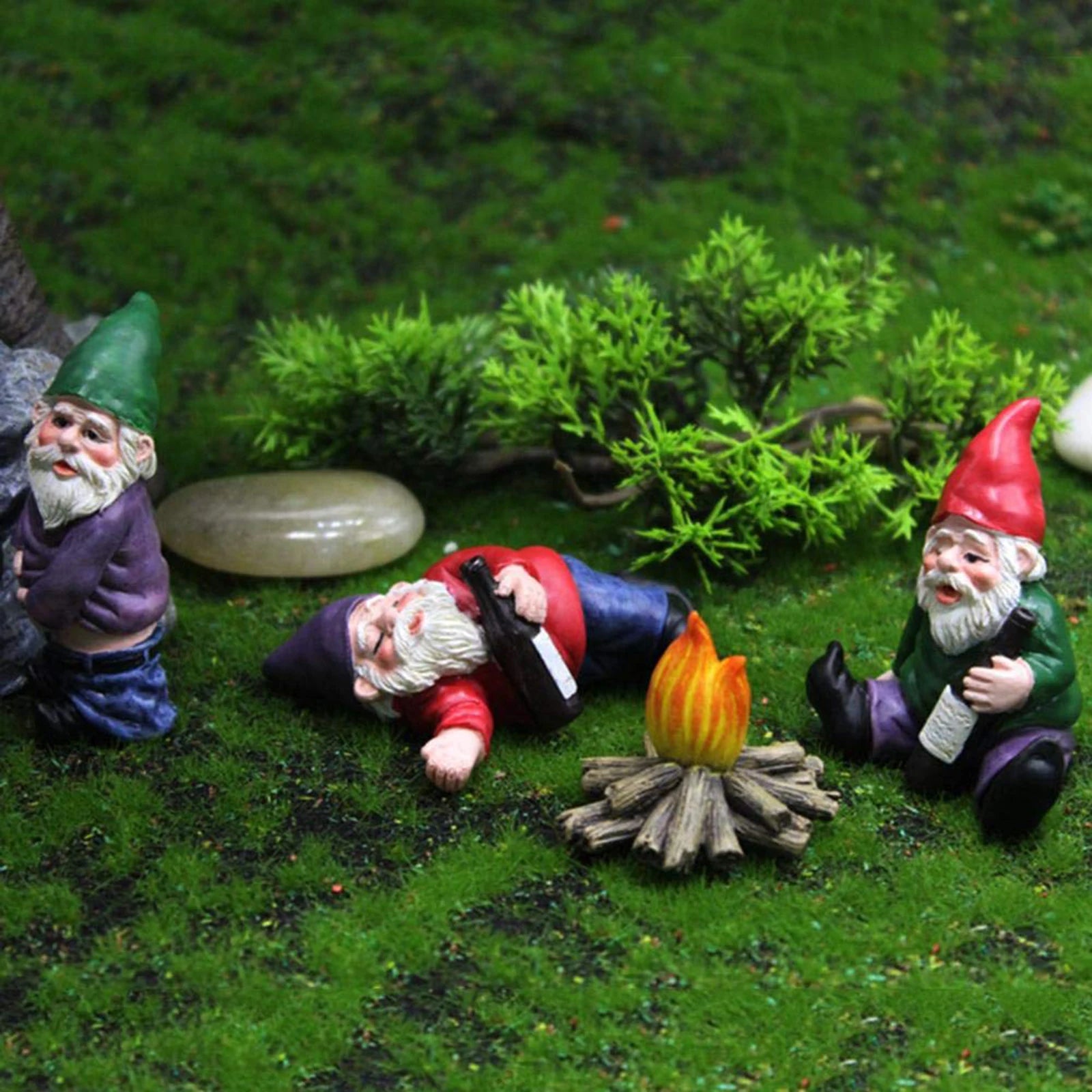 Three garden gnomes engage in playful activities around a campfire on a grassy terrain. One gnome leans against a rock, another reclines with a bottle, and the third sits holding a drink.