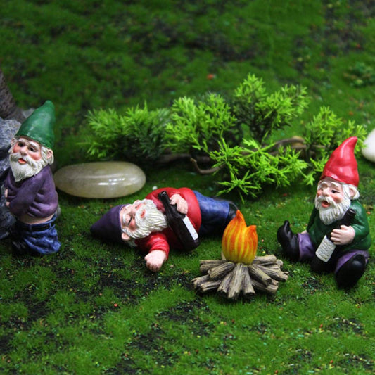 Three garden gnomes engage in playful activities around a campfire on a grassy terrain. One gnome leans against a rock, another reclines with a bottle, and the third sits holding a drink.
