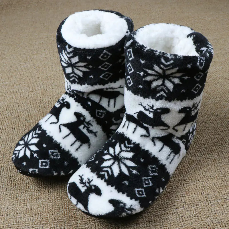Fuzzy black and white winter slippers featuring reindeer and snowflake patterns, placed on a beige carpet.