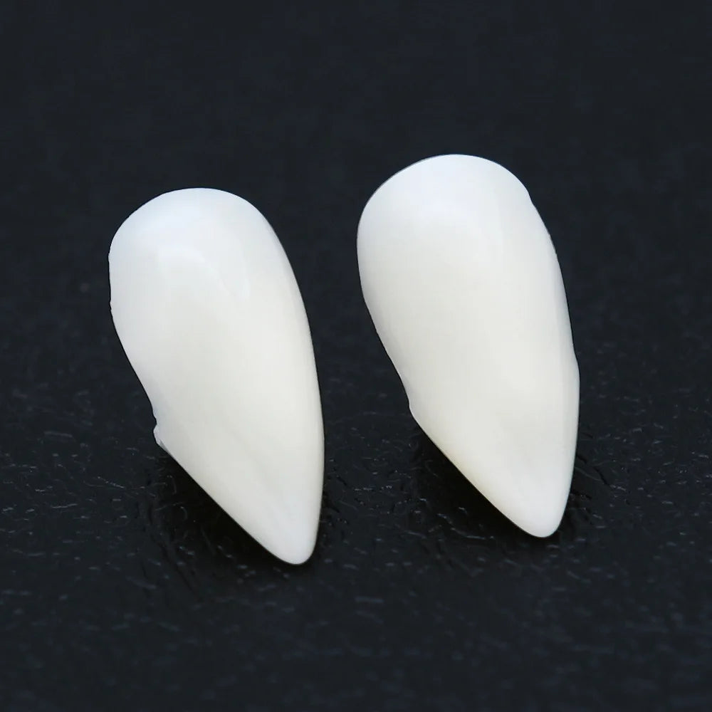 Two white, pointed fang-like teeth set on a dark background, resembling costume vampire teeth or prosthetics.