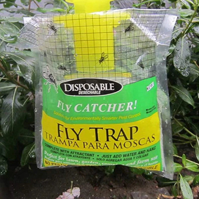 Disposable fly trap hanging among foliage, featuring a green and yellow label. Several flies are trapped inside the grid-covered bag designed for environmentally friendly pest control.