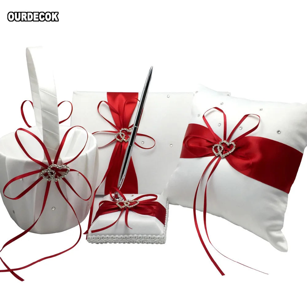 White wedding accessory set with red satin ribbons and rhinestone heart accents. Includes a basket, guest book with pen, ring pillow, and a small fabric-covered box.