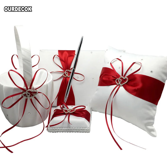 White wedding accessory set with red satin ribbons and rhinestone heart accents. Includes a basket, guest book with pen, ring pillow, and a small fabric-covered box.