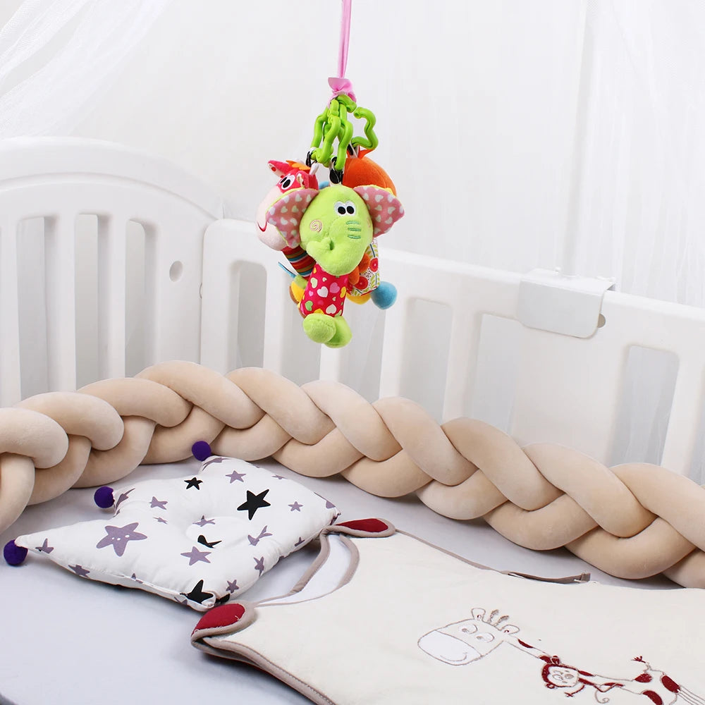 A crib with a braided bumper, star-patterned pillow, and a colorful plush toy mobile hanging above, featuring an elephant and other animals.