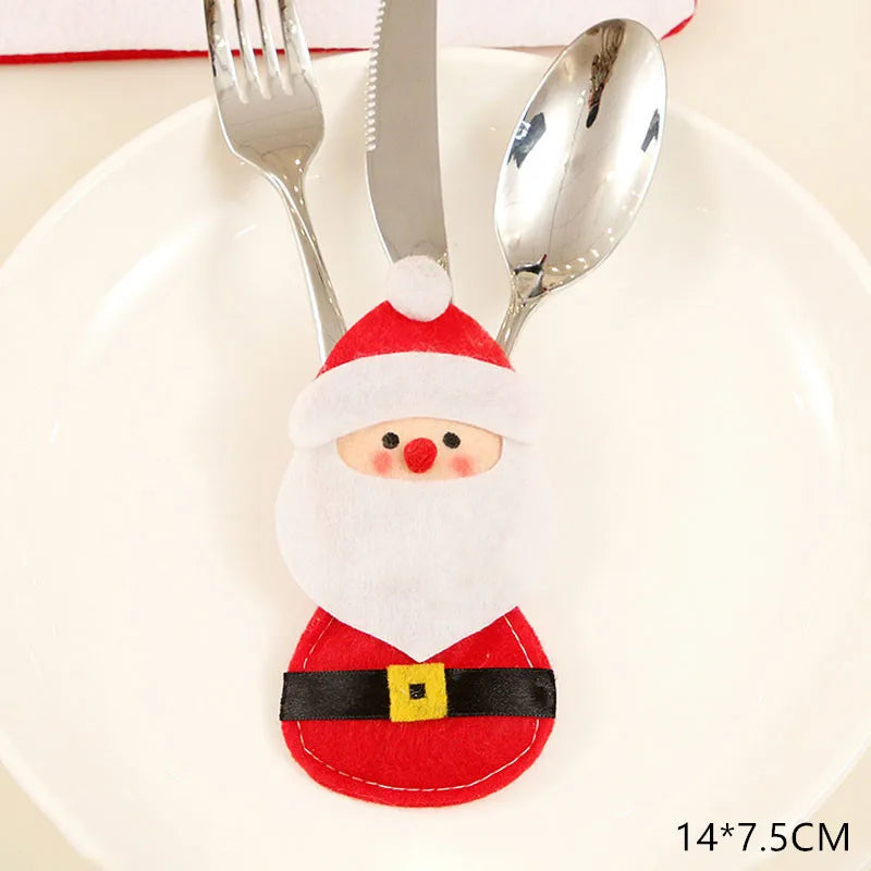 Santa-themed cutlery holder with a fork, knife, and spoon set on a white plate. The holder features a red suit, white beard, and Santa hat. Dimensions are 14x7.5 cm.