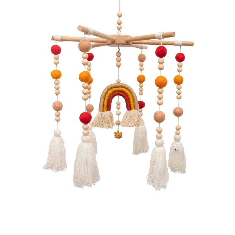 Whimsical hanging mobile with colorful felt balls, wooden beads, and a rainbow centerpiece. Features soft tassels and a small lion figure, suspended from wooden dowels.