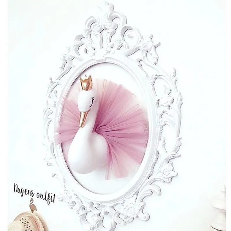 Decorative swan wall art with a golden crown and pink tulle tutu, framed in a white ornate oval frame and displayed on a light wall.