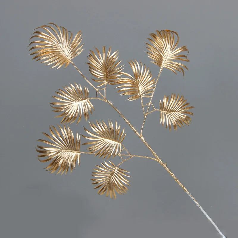 Gold metallic leaves arranged on delicate branches against a gray background, displaying an elegant, artistic design with a fan-like structure.