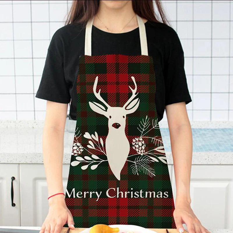 A person wearing a Christmas-themed apron with a red and green plaid pattern, featuring a white deer silhouette and pine cones. The text "Merry Christmas" is printed at the bottom.
