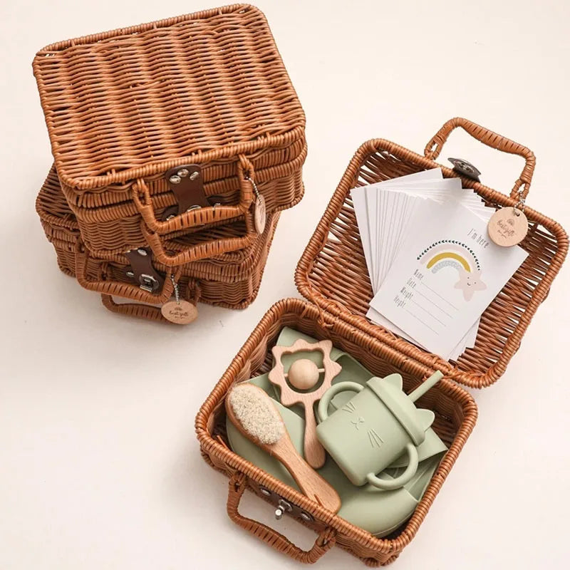 Three stacked wicker baskets, one open revealing baby items like a soft brush, teether, and green sippy cup, with a set of cards featuring a rainbow design on top.