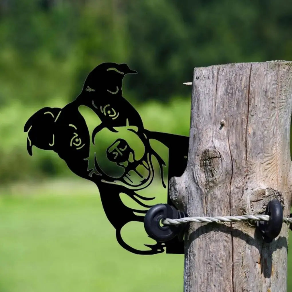 A black metal dog silhouette decorates a wooden post secured by wire. The playful design contrasts with the lush green blurred background, adding a whimsical touch to the scene.