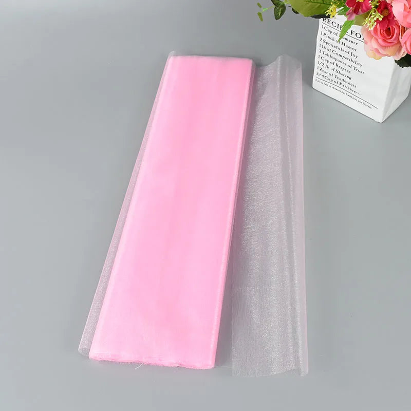 Folded pink tulle fabric on a gray surface with tulle partially unfolded. A bouquet of pink flowers in a paper vase decorates the top right corner.