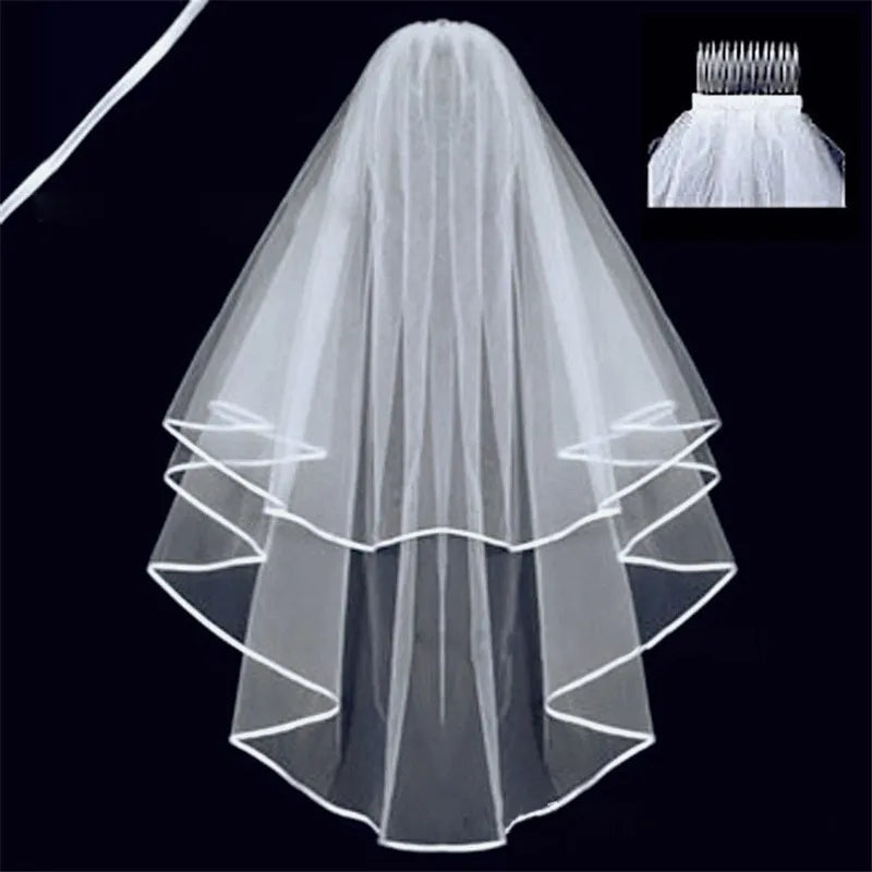 A two-tiered white bridal veil with satin trim on black background. Includes comb attachment inset in the top right corner.
