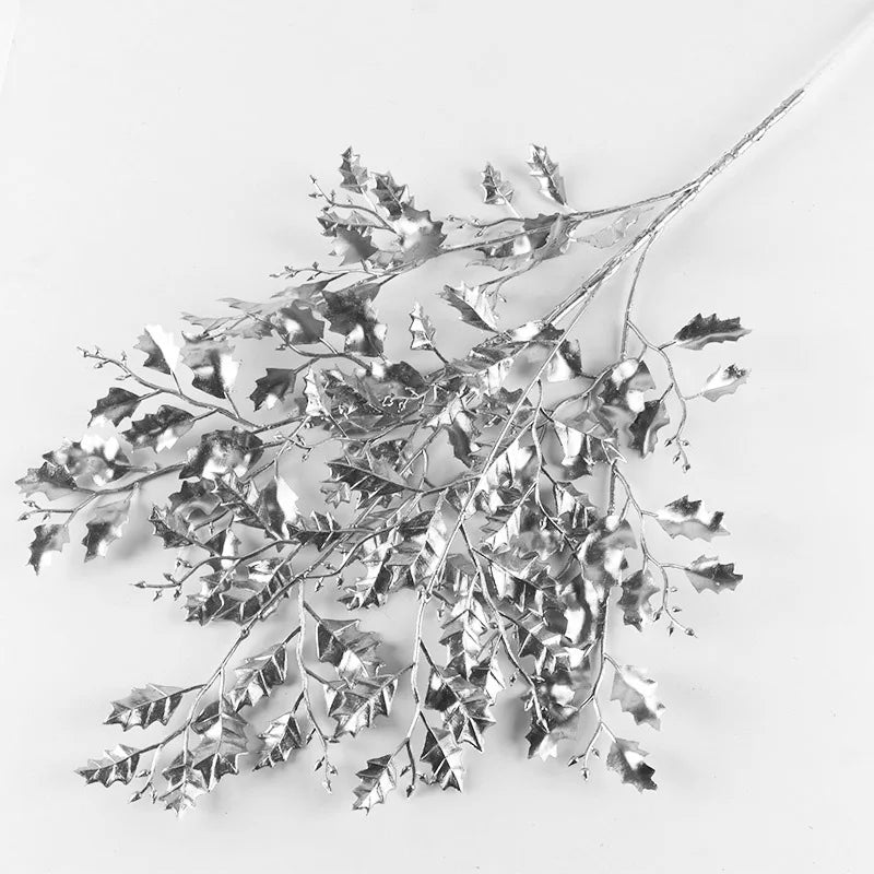 Silver metallic branches with holly-like leaves spread across a light surface, creating a textured, reflective pattern.