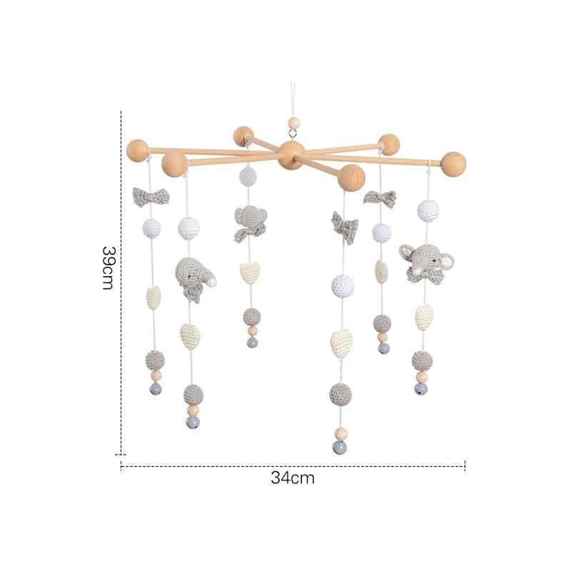 Wooden baby mobile with hanging crocheted animals and shapes in neutral tones, measuring 39cm high and 34cm wide. Features elephants, butterflies, and textured balls.