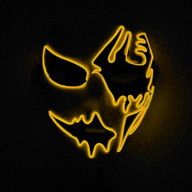 Neon mask glowing in the dark with abstract, jagged designs outlined in bright yellow. The mask features dark eye and mouth openings, creating a striking, mysterious effect.