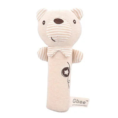 A soft beige baby rattle shaped like a bear with a striped snout and ears. It has a stitched smile, a small bow tie, and a "Gbee" label attached.