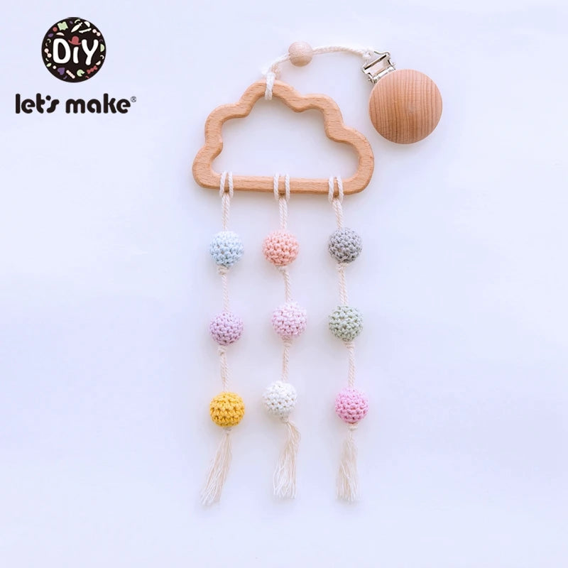 Wooden cloud-shaped mobile with pastel crochet balls hanging from strings. The design includes wooden beads and a clip for attachment. Logo "Let's Make" in the corner.