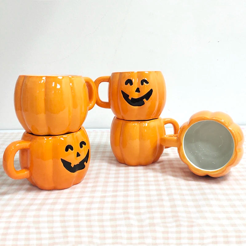 Four orange ceramic mugs with pumpkin faces are stacked in pairs on a plaid surface. One mug is lying on its side, showing its white interior.