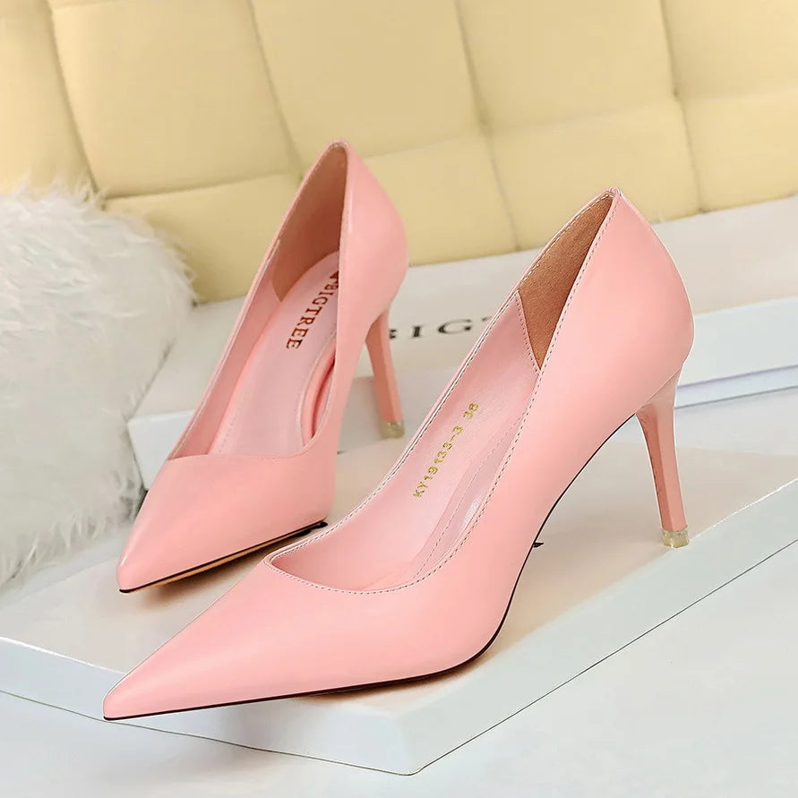 Elegant pair of pink high-heeled shoes with pointed toes, displayed on a white box against a soft background.