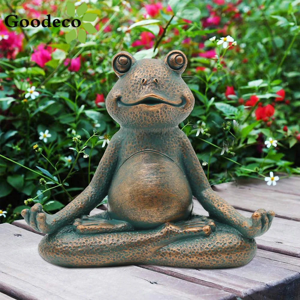 A whimsical statue of a smiling frog in a meditative pose sits on a wooden surface, surrounded by lush greenery and vibrant red and white flowers.