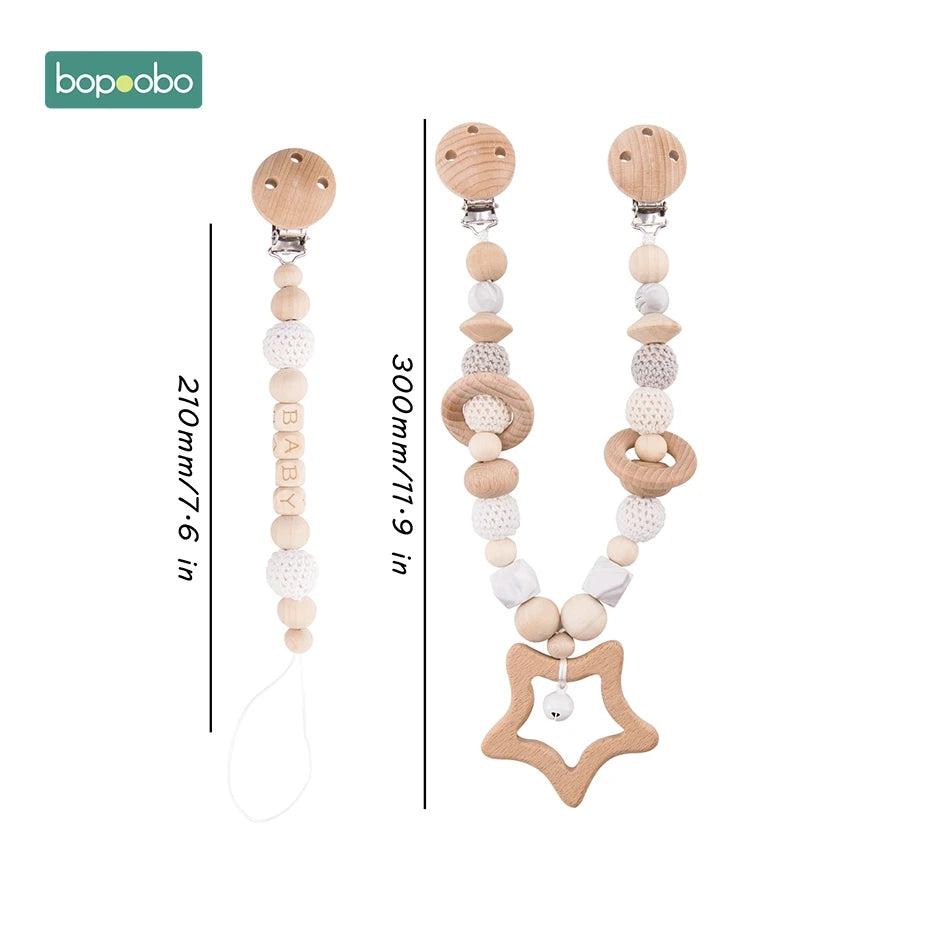 Two wooden pacifier clips, one 210mm with "BABY" beads, the other 300mm with varied textured beads and a star-shaped end. Both have wooden clips. Brand logo in the corner.