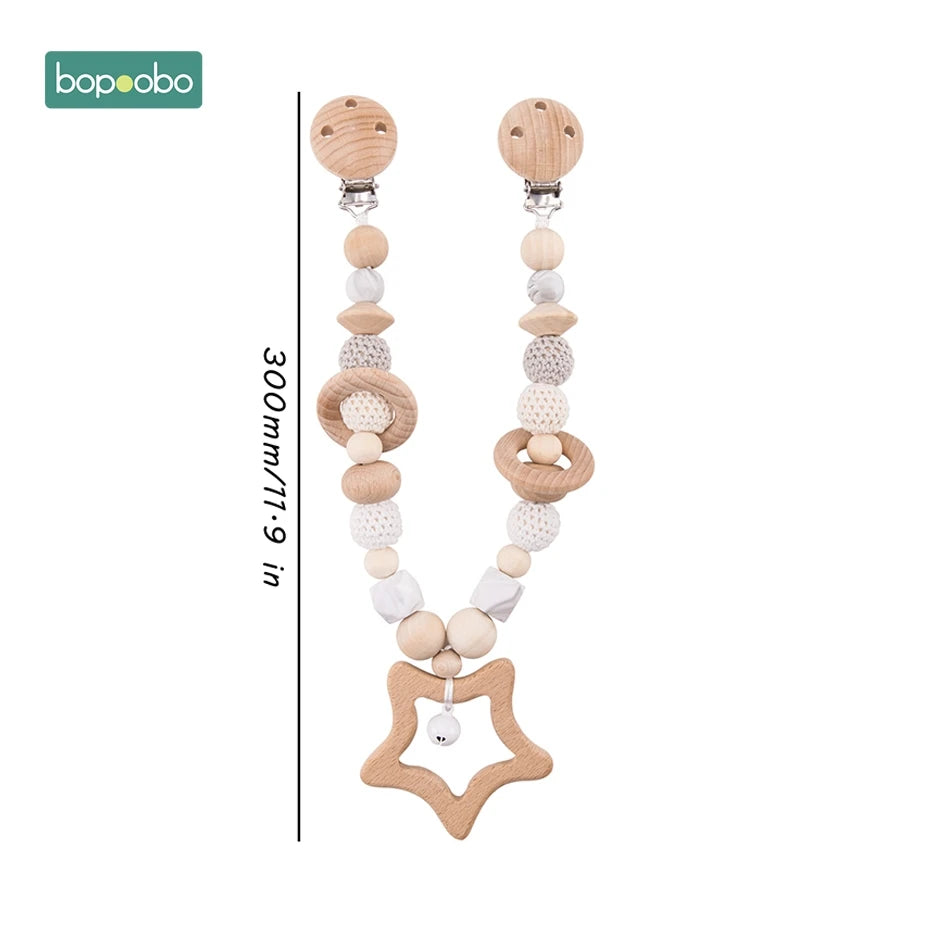 Wooden pacifier clip with varied shaped beads in natural tones, a star-shaped teether, and a bell. Approximately 300mm long. Ideal for sensory and teething relief.