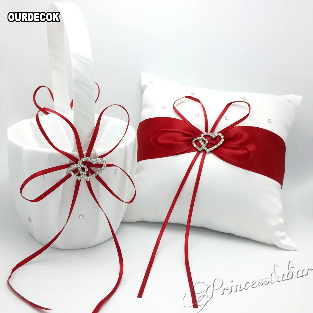 White wedding basket and pillow set with red ribbons and rhinestone heart embellishments. The pillow features small pearl-like accents, and both items coordinate elegantly.