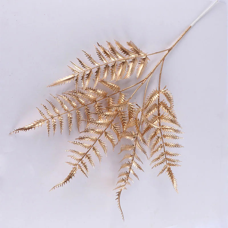 Gold fern leaves with intricate detailing on a white background, showcasing sharp, pointed edges and delicate branching, casting subtle shadows.