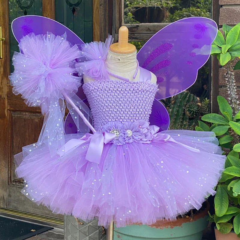 Lavender fairy costume on a mannequin with purple wings, a tulle skirt, floral sash, and a large tulle bow. Set against a wooden door and surrounded by greenery.