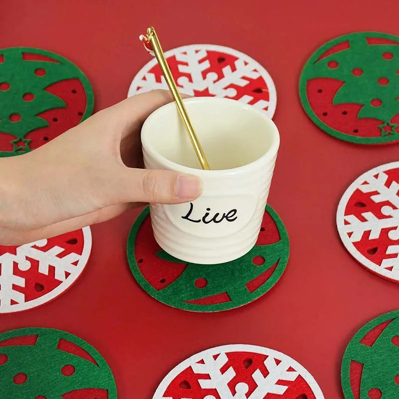 A hand places a white cup labeled "Live" with a gold stirring stick on a green and red festive coaster, surrounded by similar coasters on a red background.