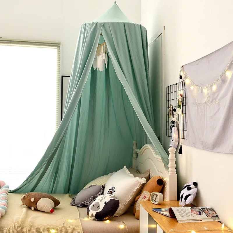 Cozy bedroom corner with a mint green canopy over a bed adorned with animal pillows. A grid wall with string lights and photos hangs above a small table with books.