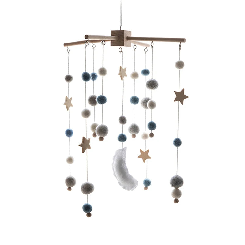 Hanging baby mobile with wooden stars, felt balls in blue, gray, and white, and a soft crescent moon, suspended from a wooden frame.