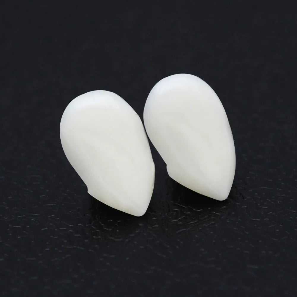 Two white teardrop-shaped earrings on a textured black surface, showcasing a smooth and glossy finish.