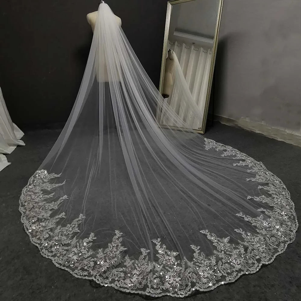 Elegant bridal veil on a mannequin with an intricate lace and sequin border, draping gracefully onto the floor. A large mirror reflects the veil's full length.
