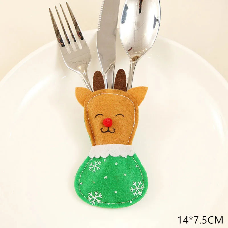 A festive cutlery holder shaped like a reindeer, with a green snowflake apron, holds a fork, knife, and spoon. It is displayed on a white plate. Size: 14x7.5cm.
