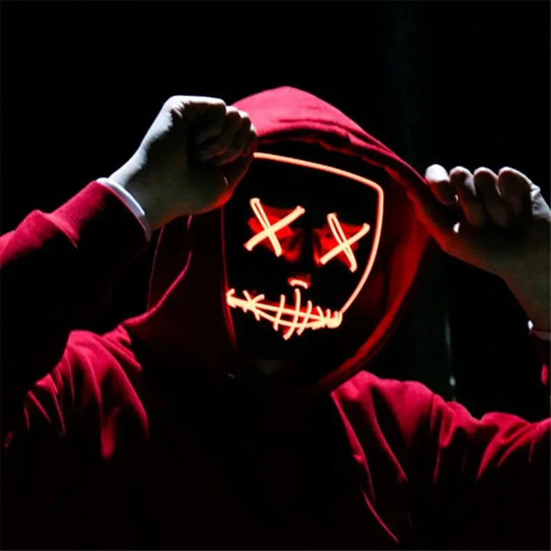Person in a red hoodie wearing a glowing LED mask with stitched mouth and X eyes design, standing against a dark background, hands pulling the hood forward.