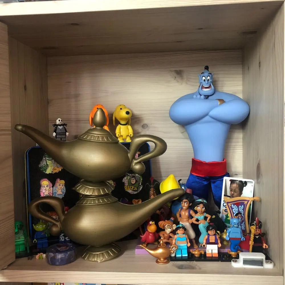 A wooden shelf displays Genie figure, two large gold magic lamps, small collectible toys, and animated character figures, including Snoopy and characters from Aladdin.