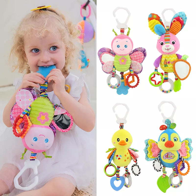 A child in a white dress plays with a colorful plush toy, shaped like a butterfly. Beside her are three more plush toys in animal shapes with rings and bright patterns.