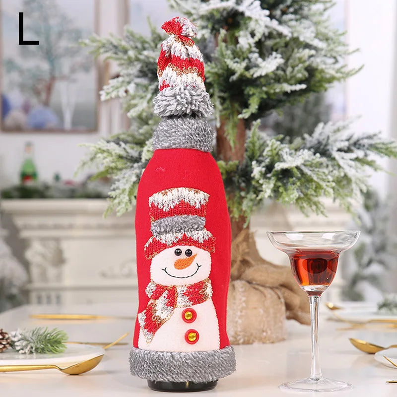 Festive bottle cover featuring a cheerful snowman with a red and gray hat and scarf, placed on a table by a glass of red wine, surrounded by holiday decor and a frosted tree.
