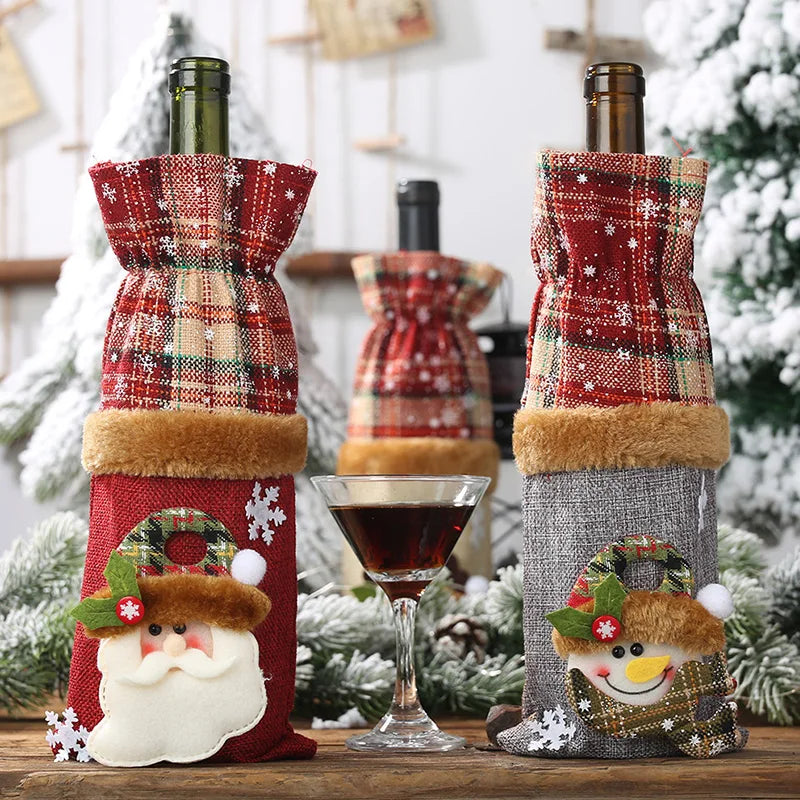 Two wine bottles in festive plaid covers, one with a Santa design and the other with a snowman. A glass of red wine is in front, with snow-covered trees in the background.
