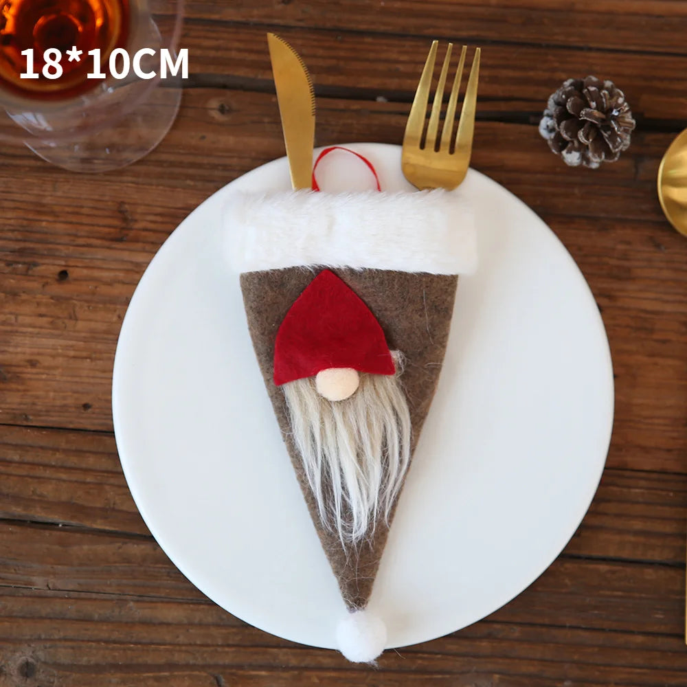 Festive cutlery holder shaped like a small Santa gnome with a red hat and white beard, placed on a white plate with a gold fork and knife on a wooden table.