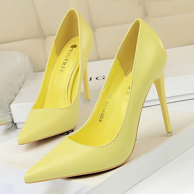 Pair of bright yellow high-heeled pumps with pointed toes, displayed on a white surface. The shoes have a sleek design and are placed with one slightly ahead of the other.